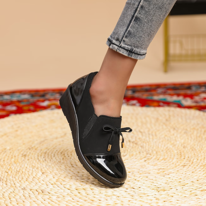 Mocassin noir verni à bout brillant, nœud sur le dessus et détail doré suspendu.