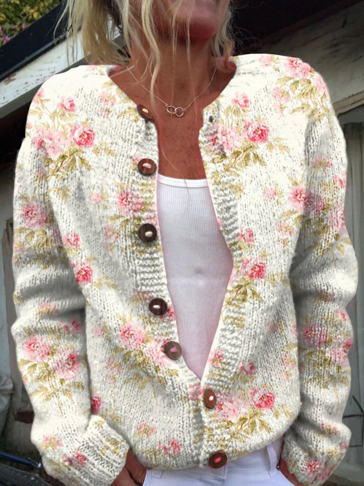 Cardigan en maille claire à boutons, décolleté en V, fleurs roses et feuilles vertes.