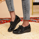 Paire de mocassins noirs vernis, nœud sur l’empeigne et semelle compensée basse.