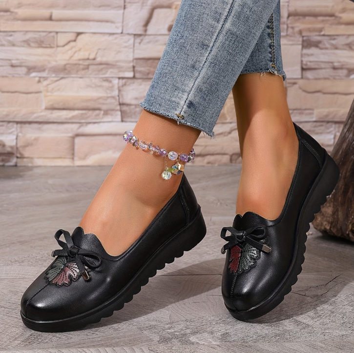 Mocassins noirs à nœud, semelle crantée, détail floral en relief sur le dessus.