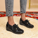 Mocassins noirs à bout brillant, nœud sur l’empeigne et semelle compensée basse.