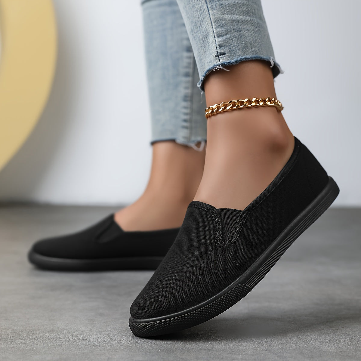 Chaussures souples à enfiler noires, chaînette dorée à la cheville, bout arrondi.