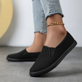 Chaussures souples à enfiler noires, chaînette dorée à la cheville, bout arrondi.
