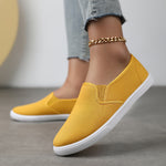 Chaussures souples à enfiler jaune moutarde, chaînette dorée à la cheville, semelle blanche.