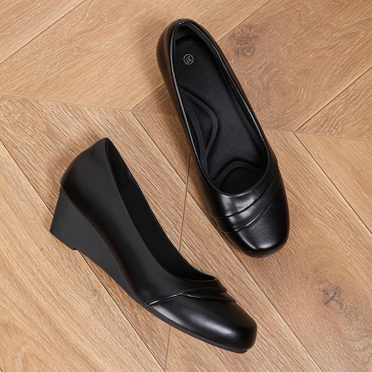 Chaussures plates noires en cuir à bout rond, profil latéral sur sol bois.