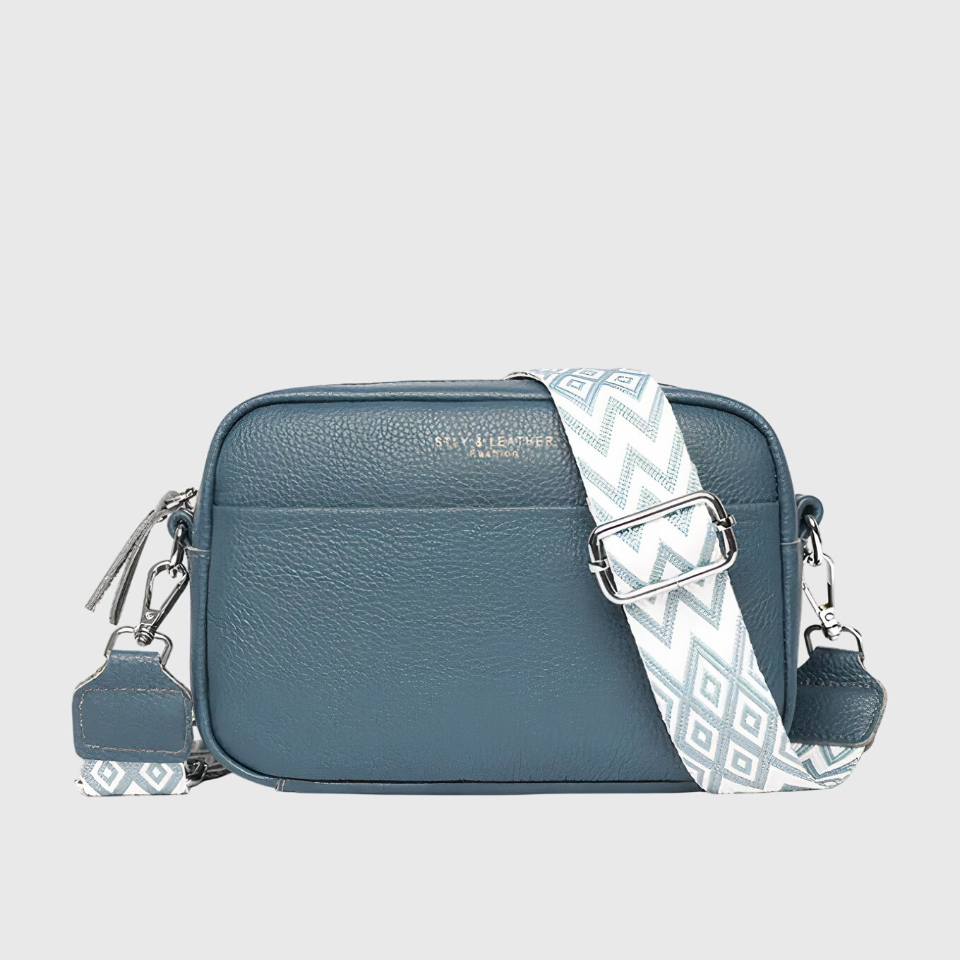 Sac à bandoulière en cuir bleu, fermeture zippée, bandoulière blanche à motif graphique.