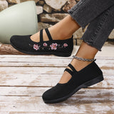 Chaussures plates noires à brides, broderie florale rose sur le dessus.
