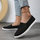 Chaussures souples à enfiler noires, chaînette dorée à la cheville, semelle blanche.