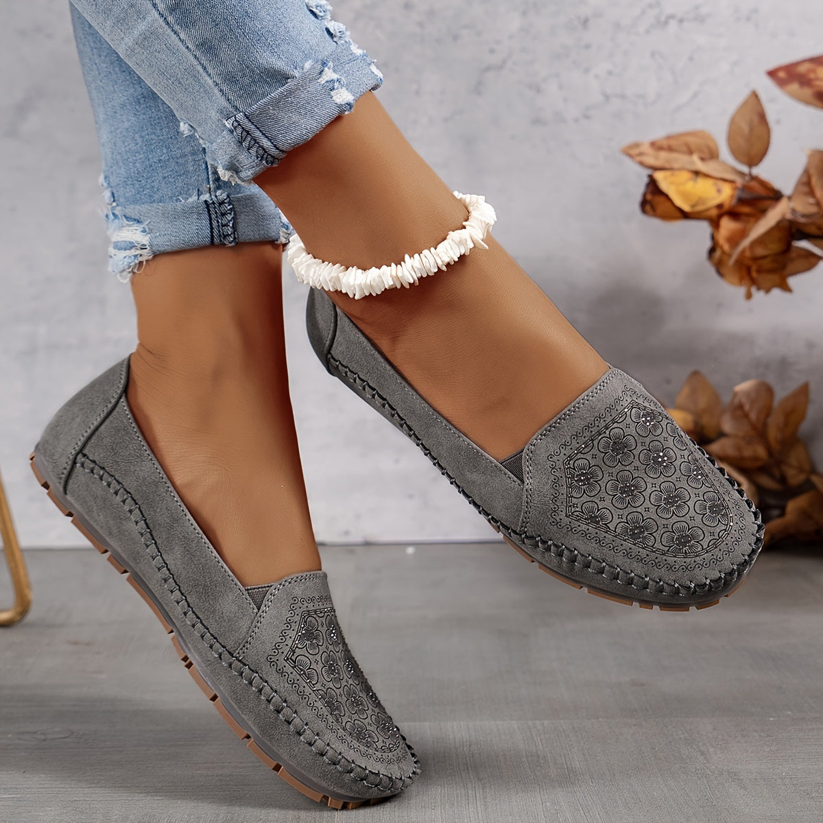 Mocassins gris ajourés avec motif floral sur l’empeigne et coutures décoratives.