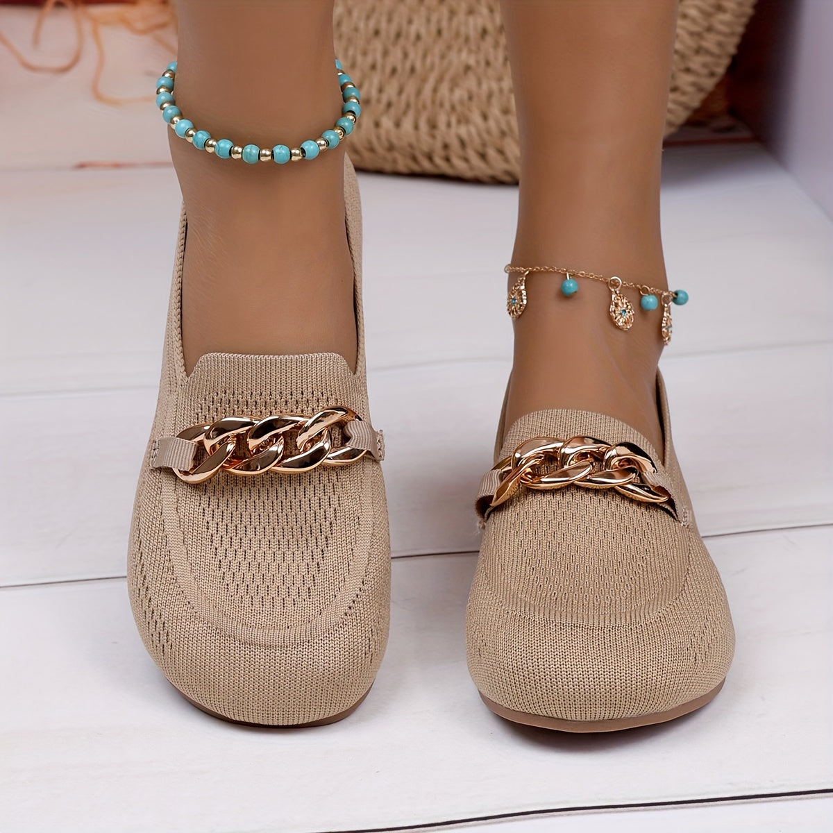 Chaussures plates beiges à empiècement tissé et chaîne dorée sur le dessus.