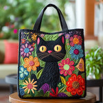 Sac cabas matelassé noir avec tête de chat brodée et fleurs colorées, anses courtes.