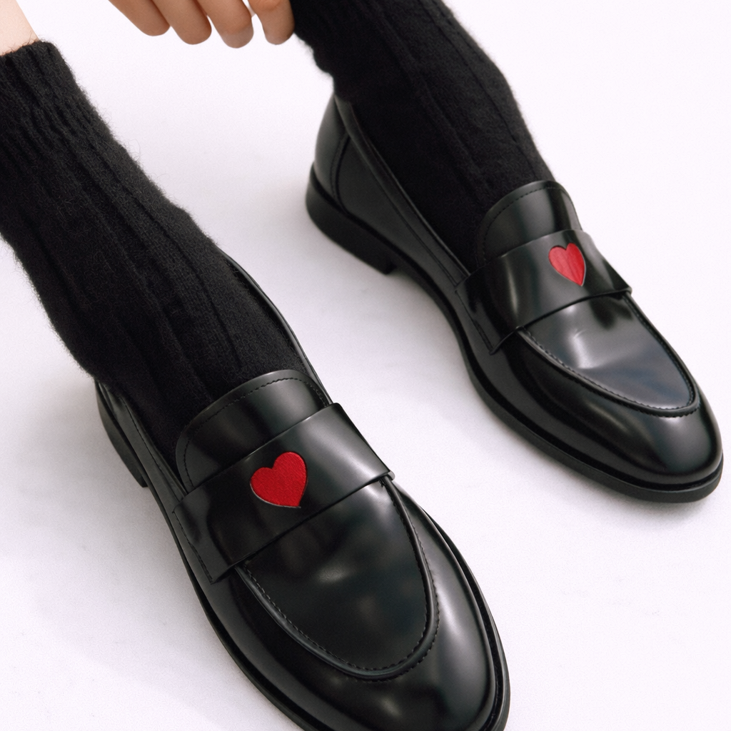 Mocassins noirs à enfiler, empiècement verni et motif cœur rouge, avec chaussettes noires.