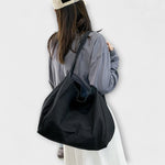 Sac cabas en toile noire, anses longues, grand format, porté à l’épaule.