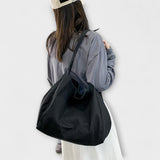 Sac cabas en toile noire, anses longues, grand format, porté à l’épaule.