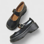 Chaussures bébé en cuir noir à bride, plateforme nervurée et surpiqûres blanches.