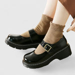Chaussures bébé en cuir noir à bride, semelle plateforme épaisse et surpiqûres claires.