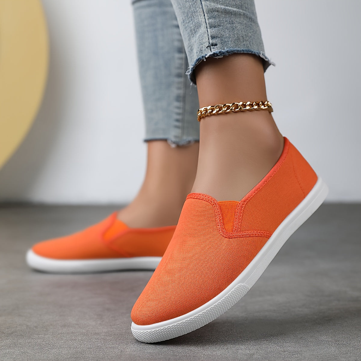 Chaussures souples à enfiler orange vif, chaînette dorée à la cheville, semelle blanche.