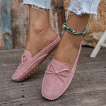 Sabots mocassin en daim rose poudré, motif perforé discret et nœud sur le bout.
