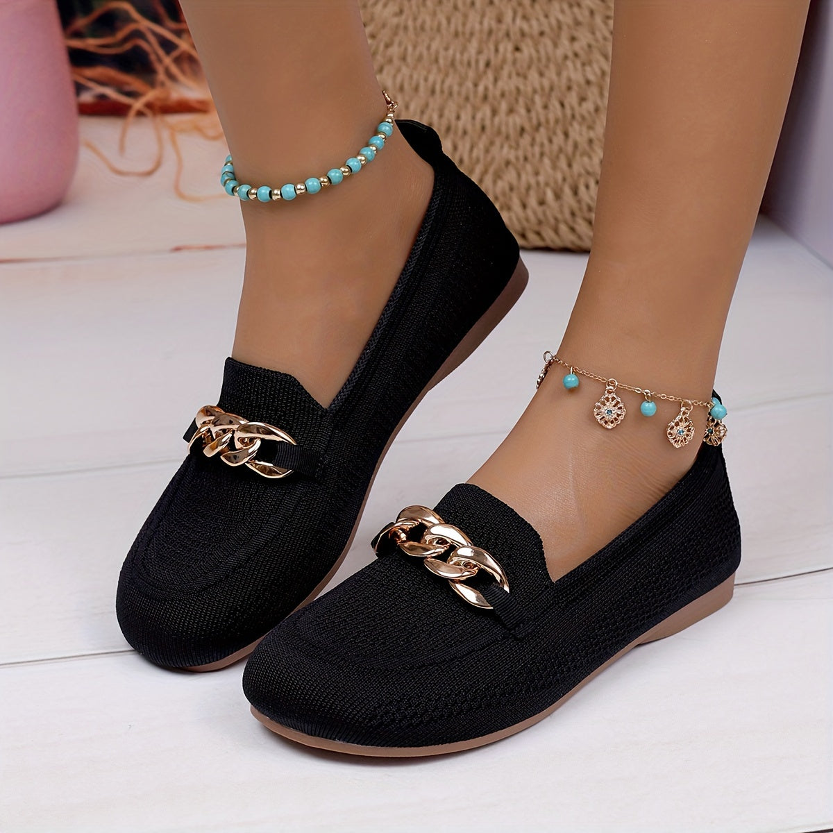 Chaussures plates noires texturées, avec chaîne dorée décorative sur l’avant.