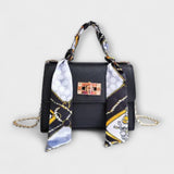 Sac à main noir avec foulard imprimé, rabat et fermoir rectangulaire, chaîne dorée.