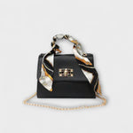 Sac à main noir avec foulard imprimé, rabat et fermoir rectangulaire, chaîne dorée.