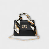 Sac à main noir avec foulard imprimé, rabat et fermoir rectangulaire, chaîne dorée.
